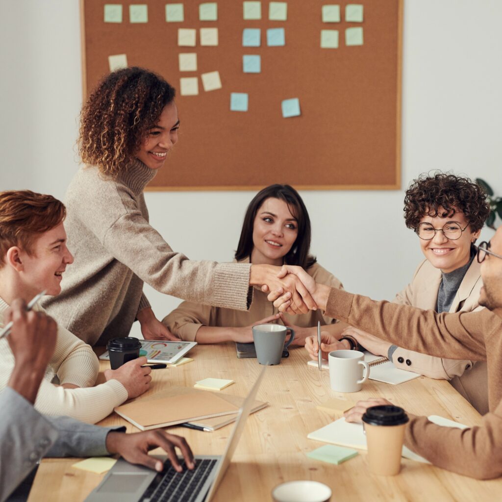 Image décorative : des employés souriant autour d'une table de réunion dont deux se sert la main